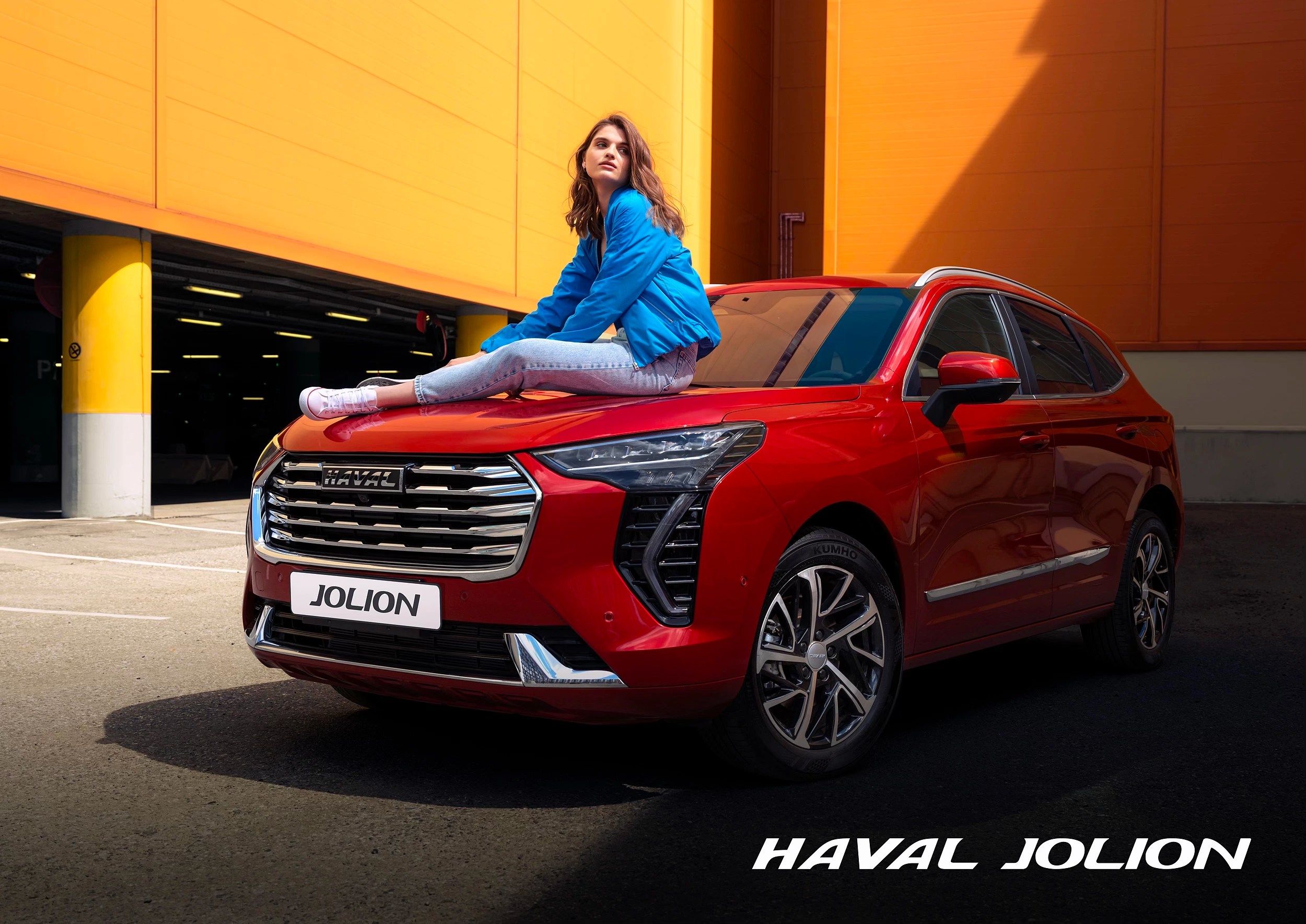 HAVAL JOLION campaign image with a woman sitting on a red SUV outside an orange building